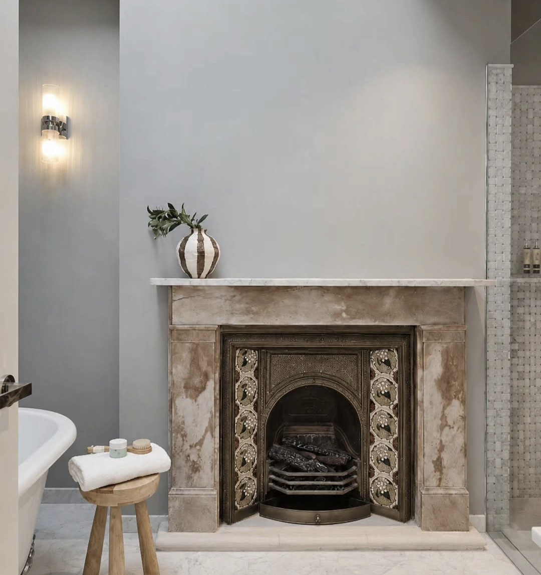 Freestanding bath beside a marble fireplace mantel styled with a ceramic vase