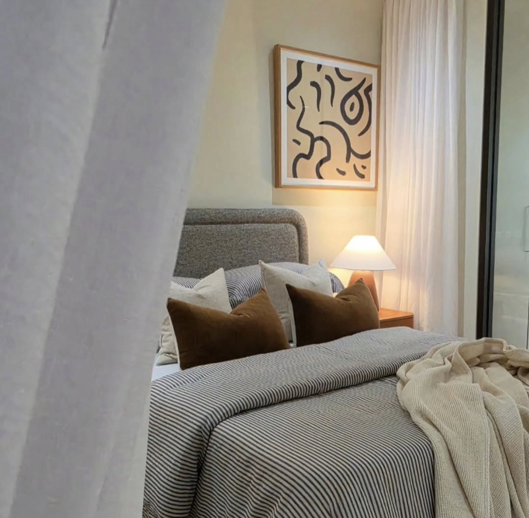 Bedroom viewed through sheer curtains with striped linen and warm bedside lighting