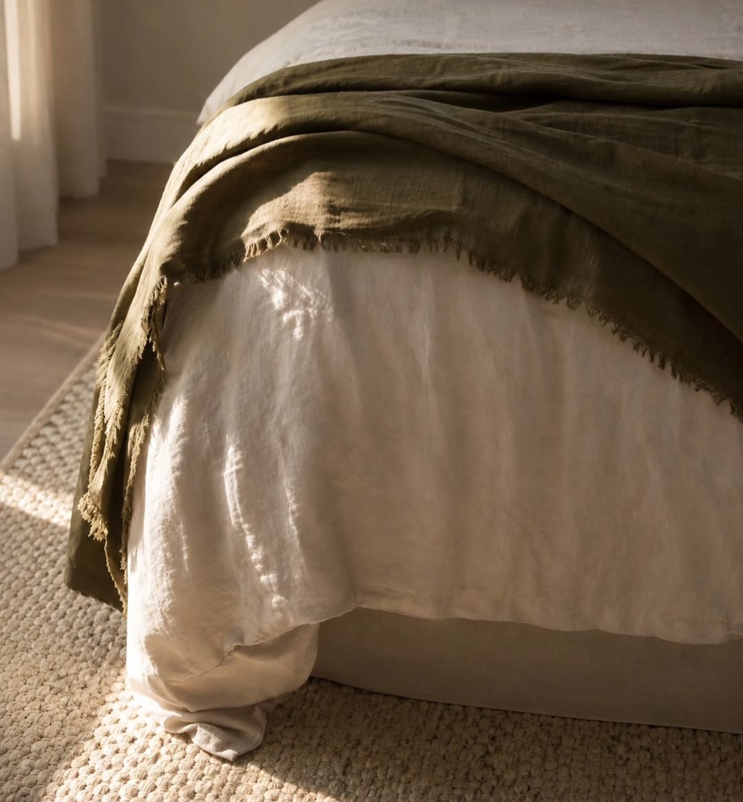 Close-up of layered linen bedding in olive and warm white on a jute rug