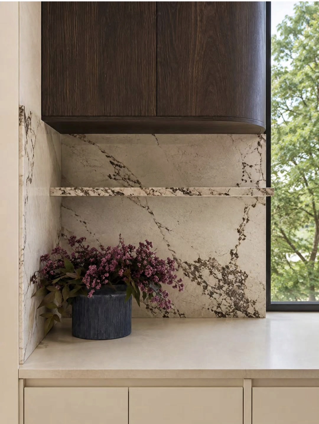 Styled kitchen corner with veined marble splashback, dark timber cabinetry and fresh flowers