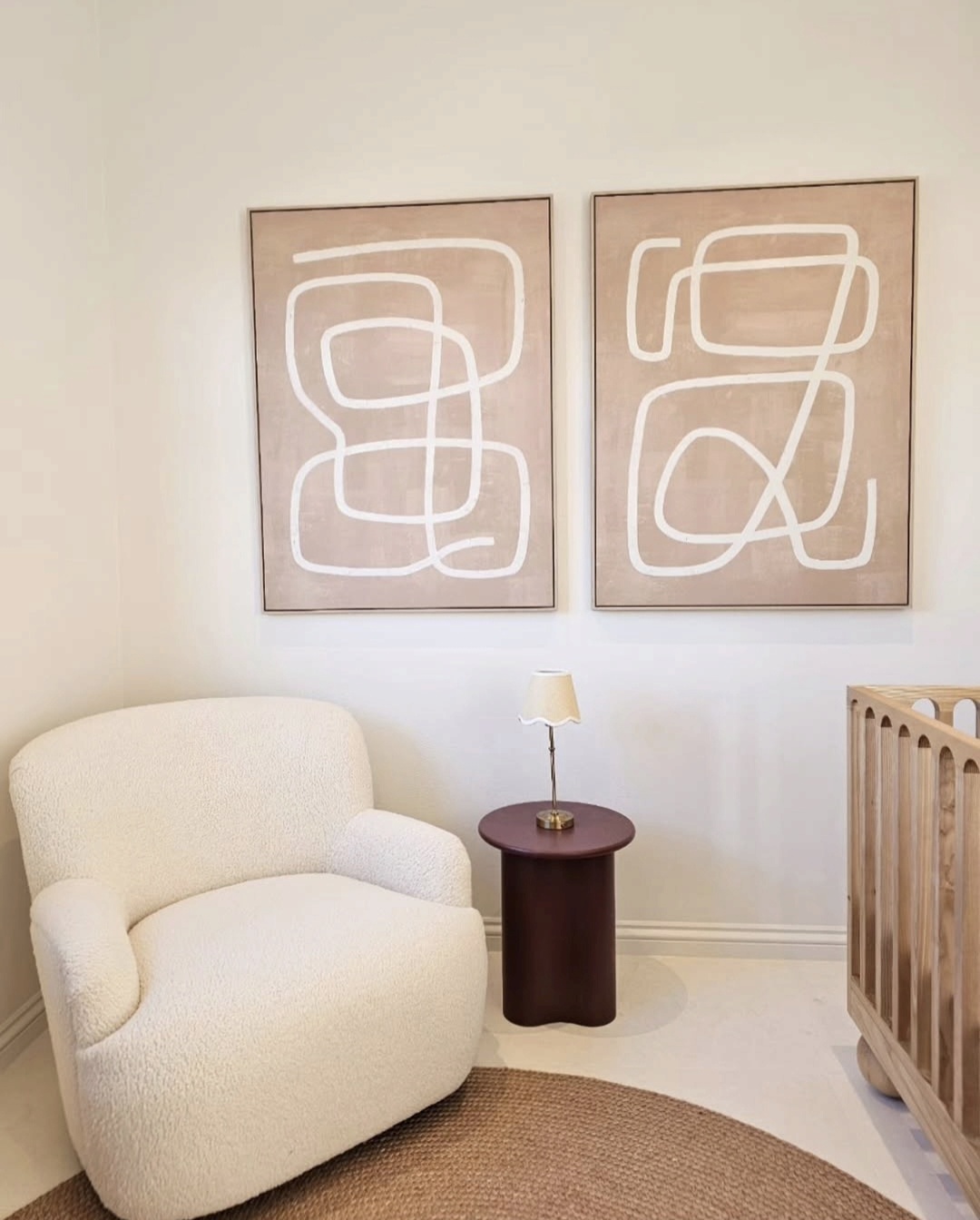 Nursery corner with boucle armchair, timber crib and a pair of abstract line artworks